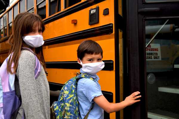 los niños suben al autobús escolar con máscaras.